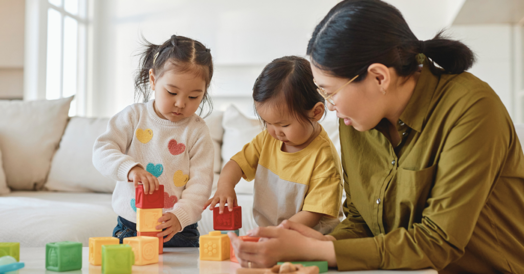 Two children playing with blocks with their mom watching by their side.